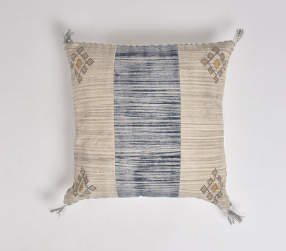 Kvadratiskt kuddfodral med beige- och blårandigt mönster, prytt med broderade geometriska detaljer i hörnen och dekorativa tofsar. Handgjort, kustinspirerat tyg som förenar traditionell och samtida stil.