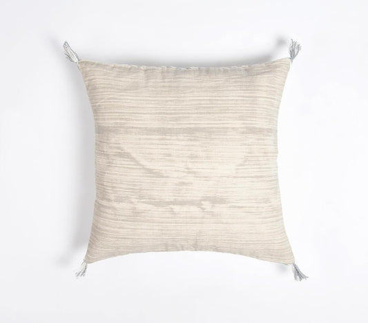 Minimalist square cushion cover in light beige with subtle texture, featuring white tassels on corners. Handcrafted cotton fabric with a hidden zipper, showcasing elegant simplicity for modern home decor.