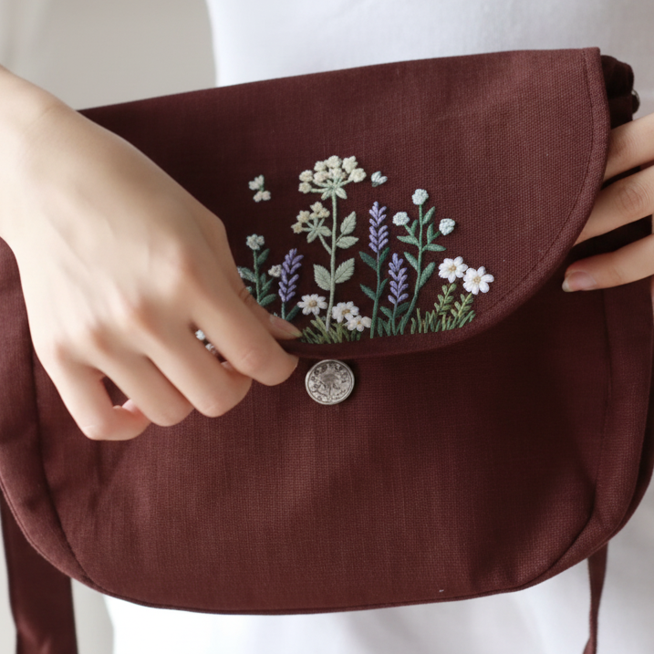 Brun necessär med blommig brodyr, hålls av en person mot en vit bakgrund